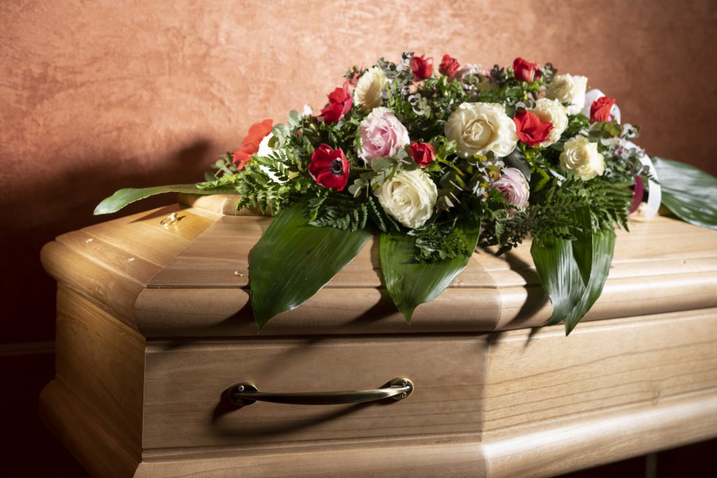 Composizione di rose bianche e rosa, anemoni rossi e felci su una bara in legno chiaro con maniglia dorata